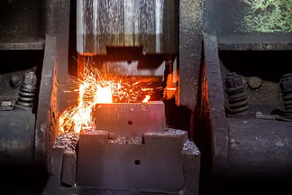 Forging hammer hitting a hot piece of metal