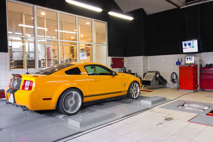A yellow automobile sits on top of a chassis dyno for testing