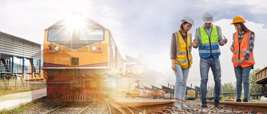 A group of engineers stand beside a train discussing how to fix the track.